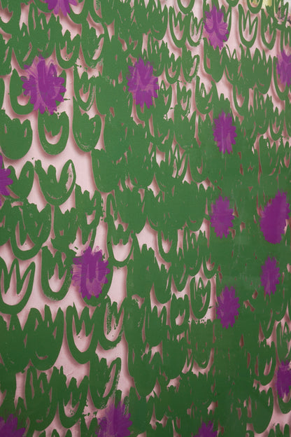 “Tableau contemporain coloré représentant un chien dans un champ fleuri vert et violet, posé sur un chevalet dans un atelier lumineux avec une table en bois et une tasse illustrée au premier plan.”